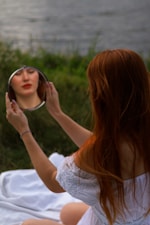 a woman sitting on a blanket looking at her reflection in a mirror