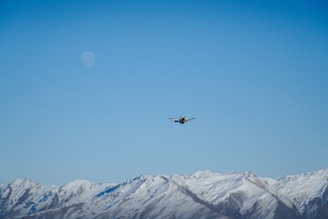 A sleek drone flying over a clear blue sky with mountains in the background.