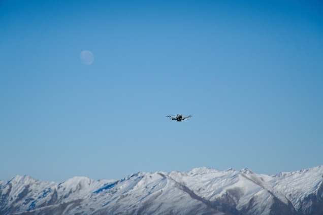 A sleek drone flying over a clear blue sky with mountains in the background.