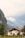 A picturesque white house with a red-tiled roof situated amidst lush greenery, with a backdrop of towering mountains partially shrouded in mist.