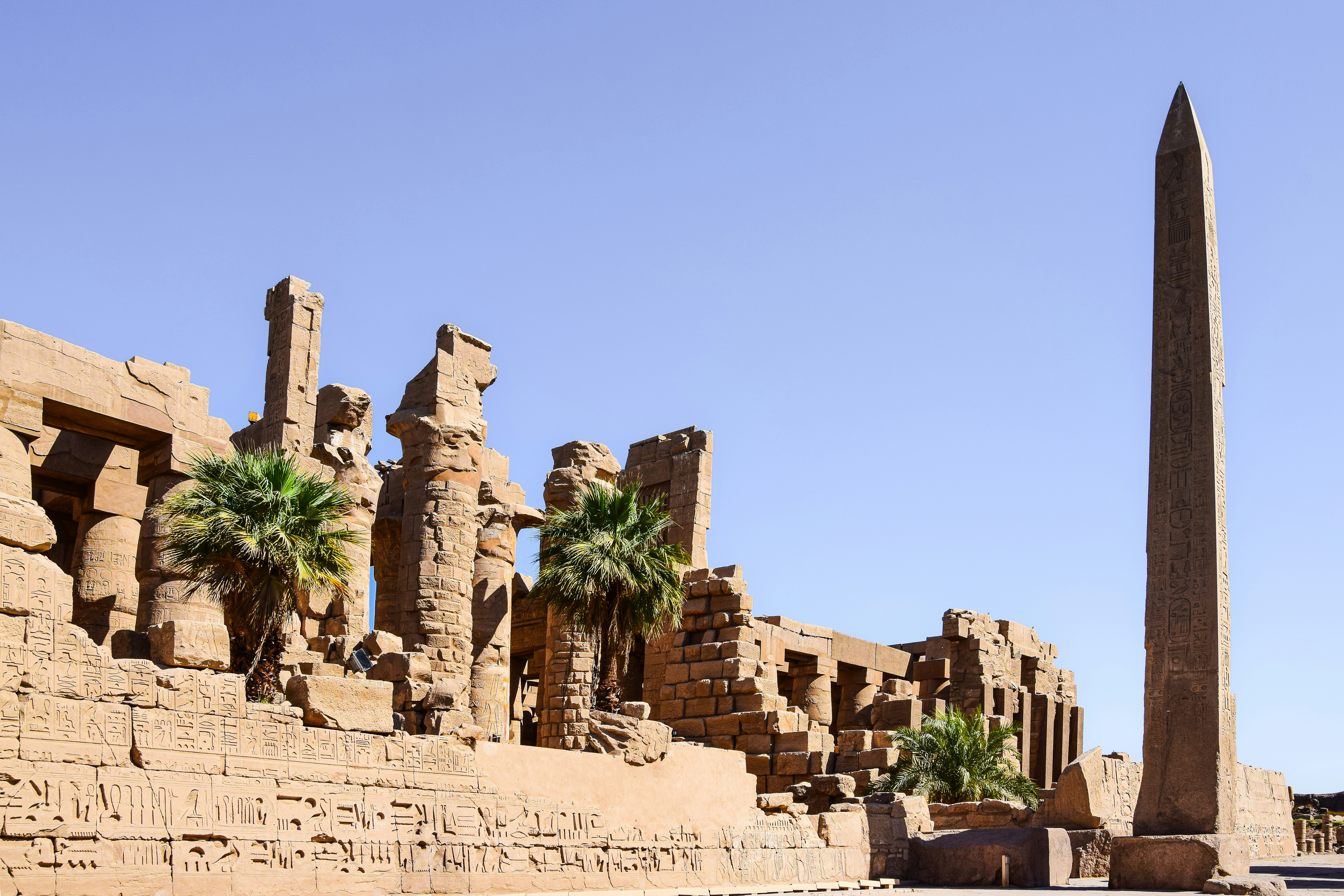 a tall obelisk in front of a building with palm trees, Luxor, Egypt.