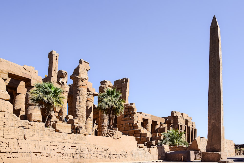 a tall obelisk in front of a building with palm trees