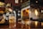 A bottle of Johnnie Walker Green Label is prominently placed on a wooden bar counter. A glass with ice cubes is being filled with the same whisky from another bottle. The bar setting is cozy, featuring dim lighting and a brick wall in the background, with several decorative elements such as framed pictures and hanging lights.