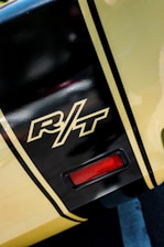 Close-up of a section of a vehicle with a glossy black and yellow paint job. The letters 'R/T' are prominently featured in a stylized font. The area also includes a small red light fixture.
