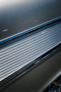 Detailed image of a metallic surface with horizontal grooves, reflecting light. The texture appears smooth with a sleek, modern design.