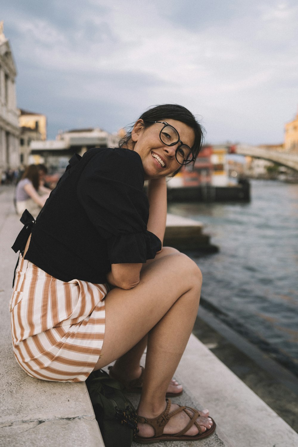 a woman sitting on a ledge next to a body of water