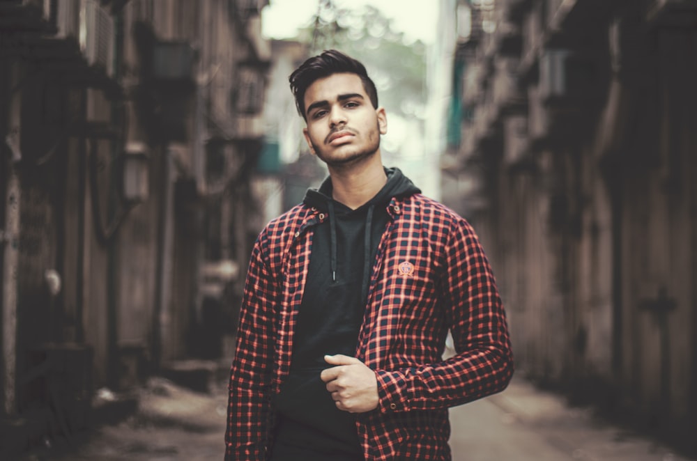 a man in a red and black checkered jacket standing in an alley way