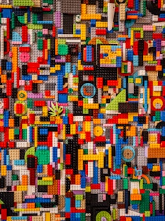 An intricate mosaic of interlocking LEGO pieces in various shapes and sizes, arranged in a colorful and chaotic pattern. The bricks come in a wide array of colors including red, blue, yellow, green, and more, creating a vibrant and visually complex scene.