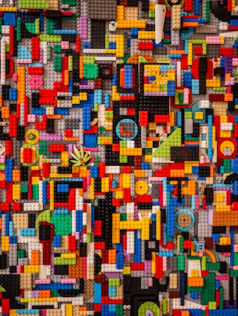 An intricate mosaic of interlocking LEGO pieces in various shapes and sizes, arranged in a colorful and chaotic pattern. The bricks come in a wide array of colors including red, blue, yellow, green, and more, creating a vibrant and visually complex scene.