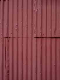Corrugated metal sheets painted in a faded reddish-brown color with visible seams and texture. Each sheet is vertically aligned with visible rust spots and dents, giving a rugged, industrial appearance.