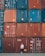 A person stands casually in front of a large stack of colorful shipping containers. The containers are organized in neat rows, featuring hues of red, blue, and orange. Each container has various labels and markings typically seen in industrial settings.