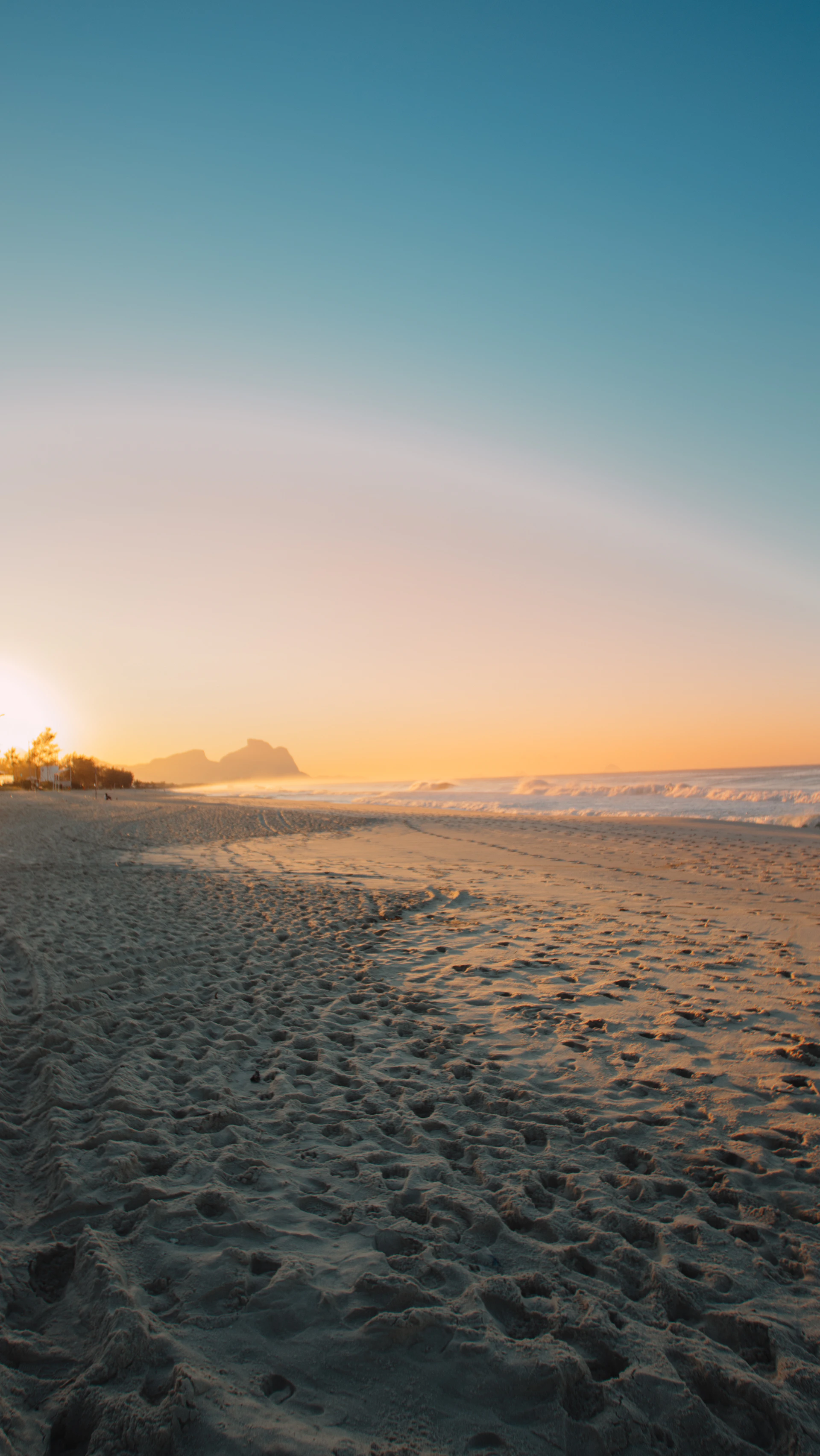 the sun is setting on the beach with footprints in the sand