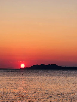 Golden sunset casting warm light over calm sea with silhouetted islands.