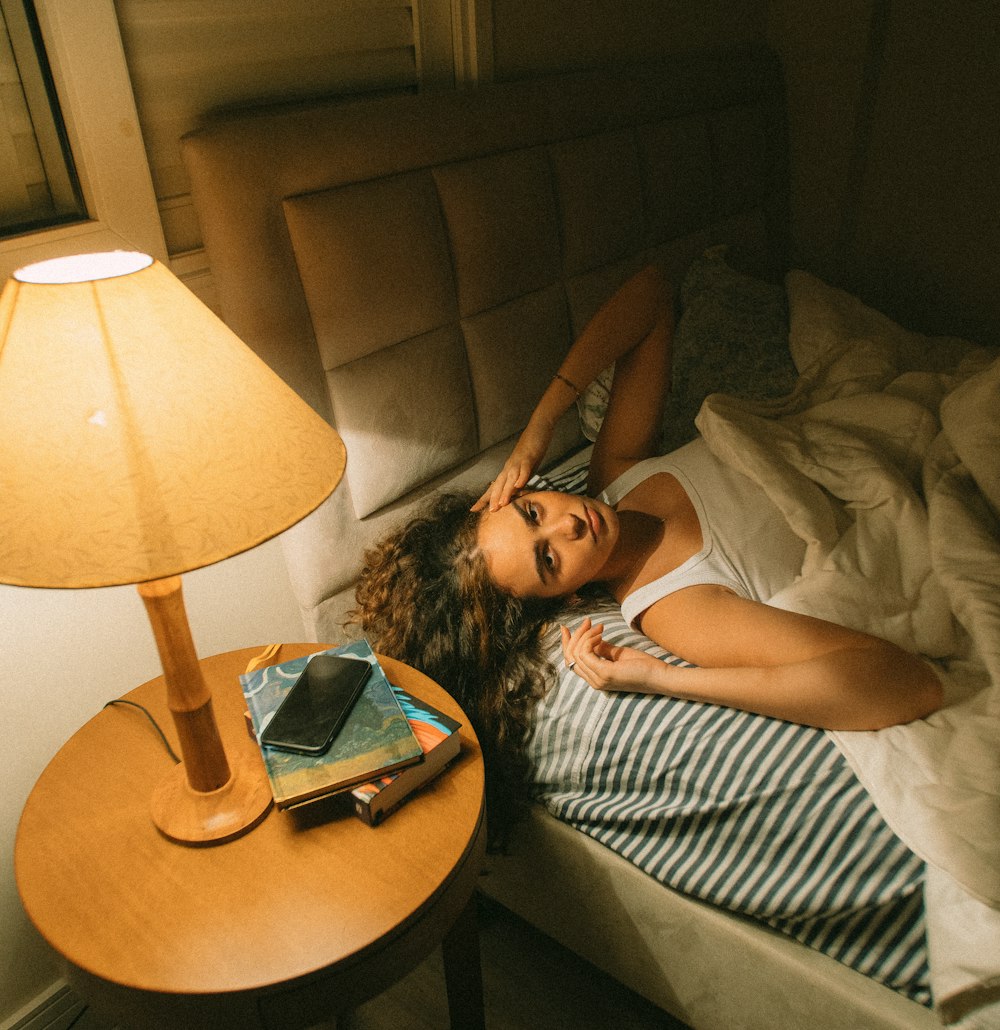 a woman laying on a bed next to a lamp