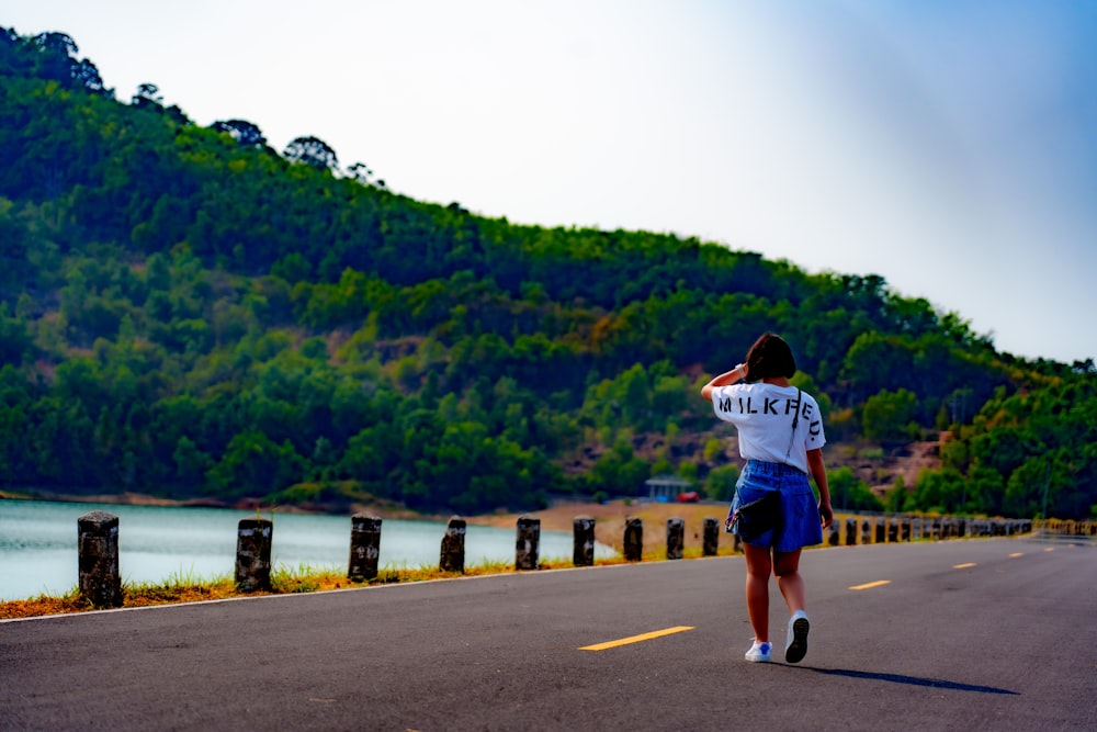 a woman walking down a road next to a lush green hillside