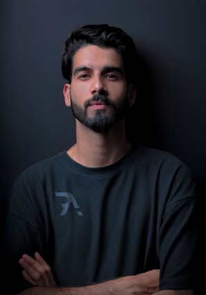 a man with his arms crossed standing in front of a black wall