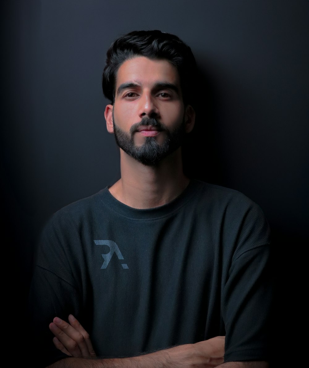 a man with his arms crossed standing in front of a black wall