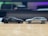 Two scale model cars are positioned facing each other on a smooth wooden surface. The car on the left is black, while the one on the right is silver. The background is blurred, highlighting the models.