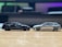 Two scale model cars are positioned facing each other on a smooth wooden surface. The car on the left is black, while the one on the right is silver. The background is blurred, highlighting the models.