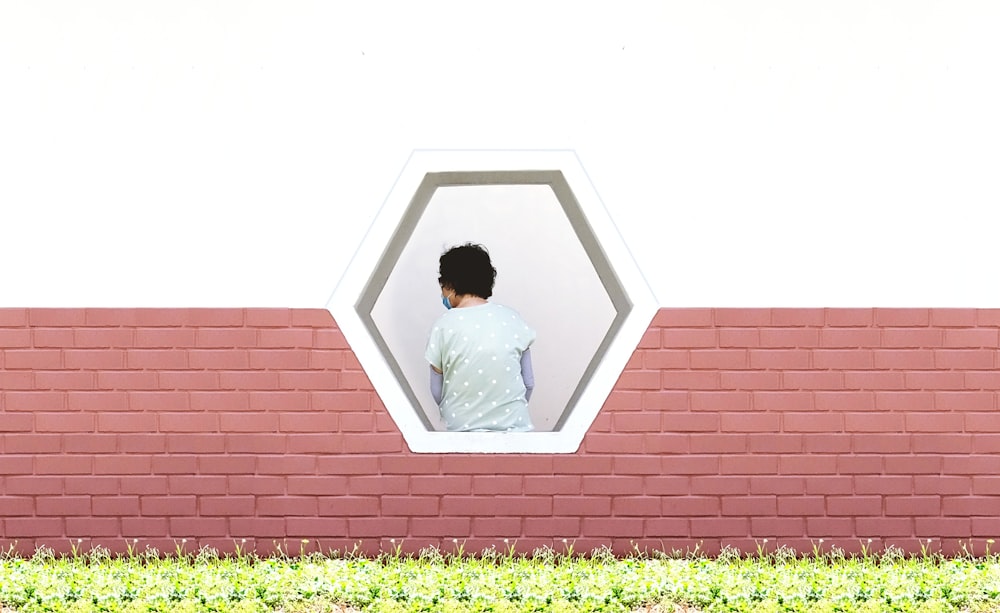 um homem olhando por uma janela em uma parede de tijolos