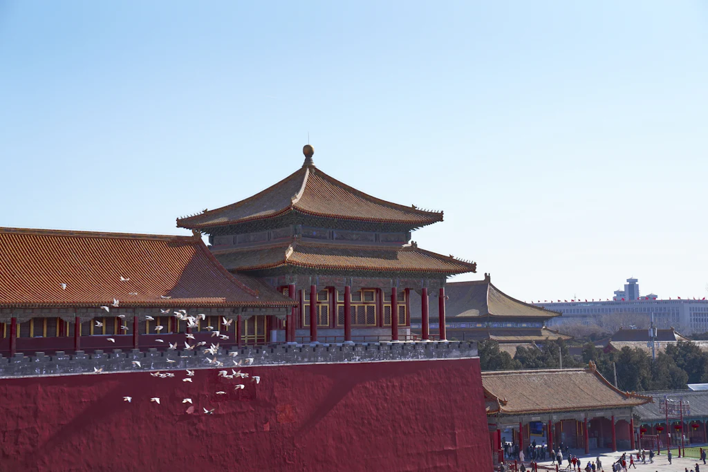 Red palace walls and tiled halls of the Forbidden City in Beijing, with white birds crossing the foreground