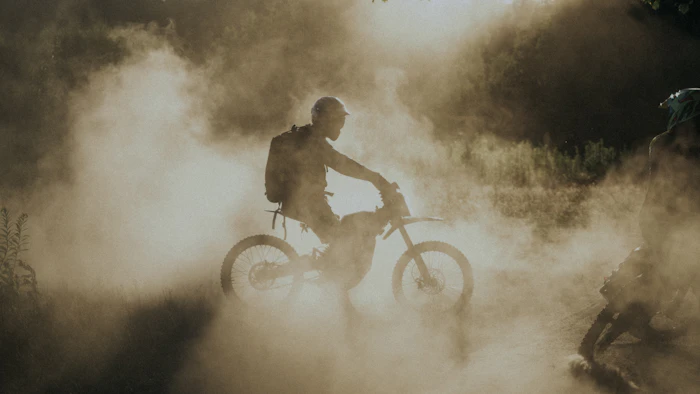 Silhouette of a rider on an electric dirt bike in dust at dawn