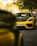A yellow sports car is parked on a cobblestone street under a tree. The car's license plate reads 'PY 40084'. The environment is urban with buildings and streetlights in the background. The scene has a sunny ambiance, with sunlight filtering through the leaves.