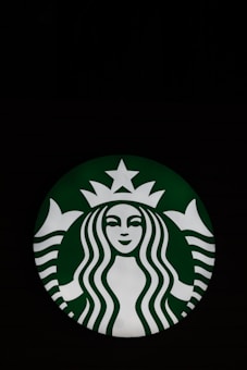 A circular logo featuring a stylized illustration of a mermaid with flowing hair, a crown, and a star above her head. The mermaid is depicted in white on a green background.