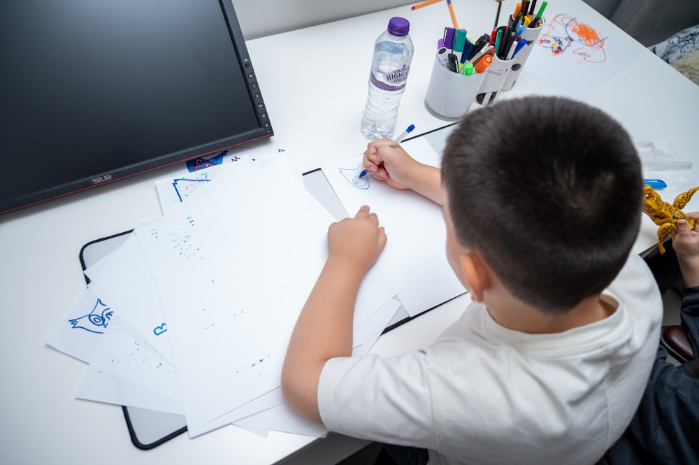 a young boy sitting at a desk drawing on a piece of paper