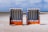 Two striped blue and white beach chairs are placed on a sandy shore under a cloudy sky. The chairs are positioned side by side, facing the open beach and the distant ocean horizon.