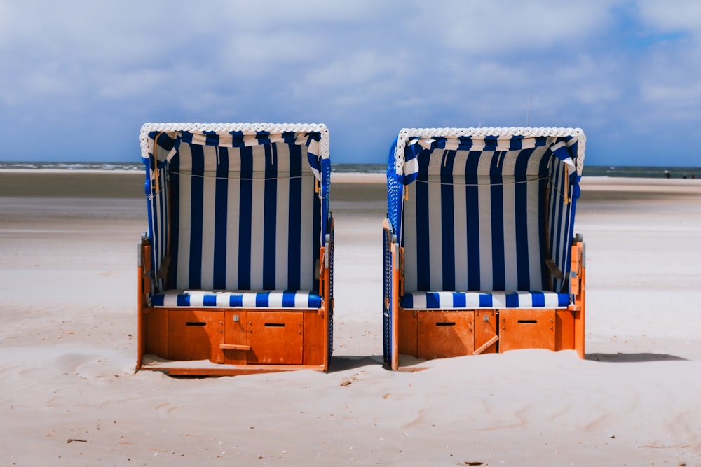 two blue and white striped chairs sitting on top of a sandy beach