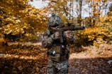 a man in camouflage holding a rifle in a wooded area