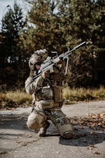 a man in camouflage holding a rifle while kneeling down