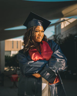 A doctoral graduate in an elegant gown and cap, standing confidently in a formal setting.
