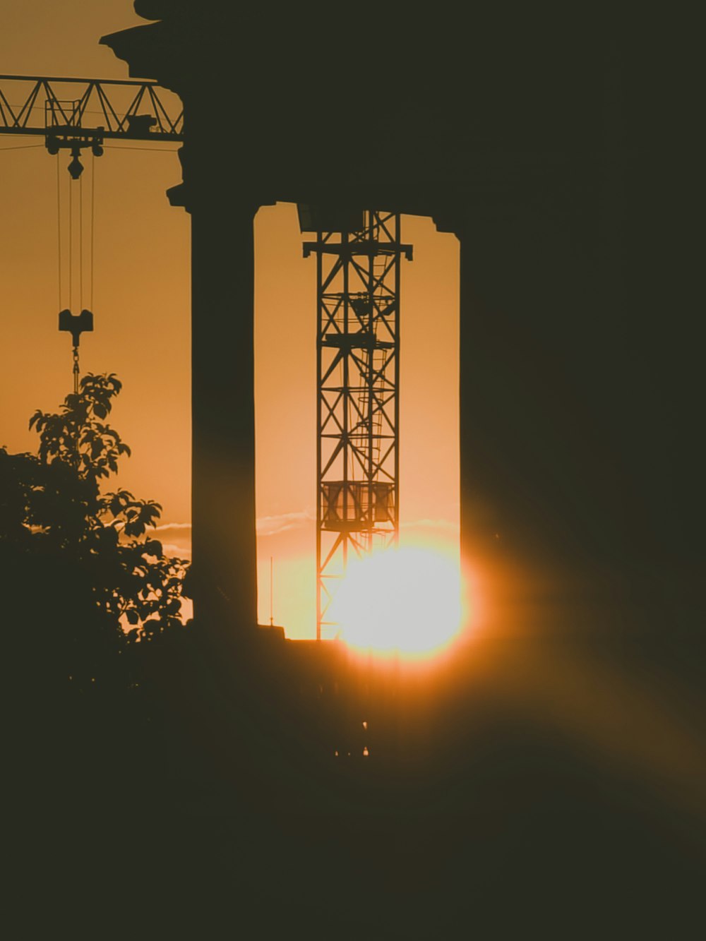 the sun is setting behind a tower crane