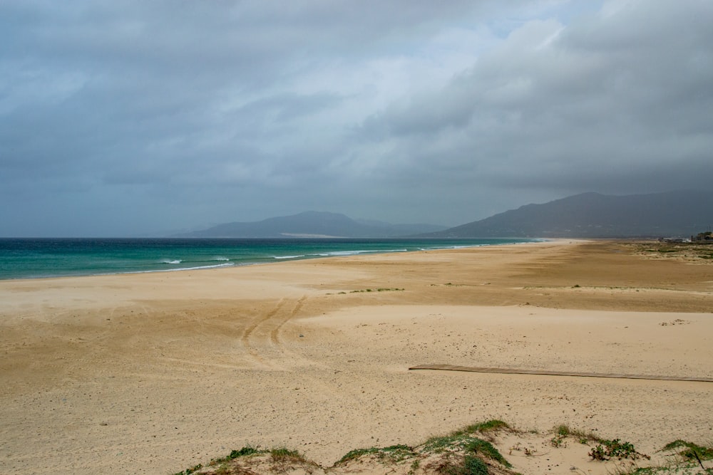 a sandy beach on a cloudy day with blue water