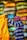A person wearing a striped shirt and a pink and white checkered headscarf is handling a large yellow sack. Behind them, there are stacks of colorful bags in various shades of yellow, orange, blue, and gray.
