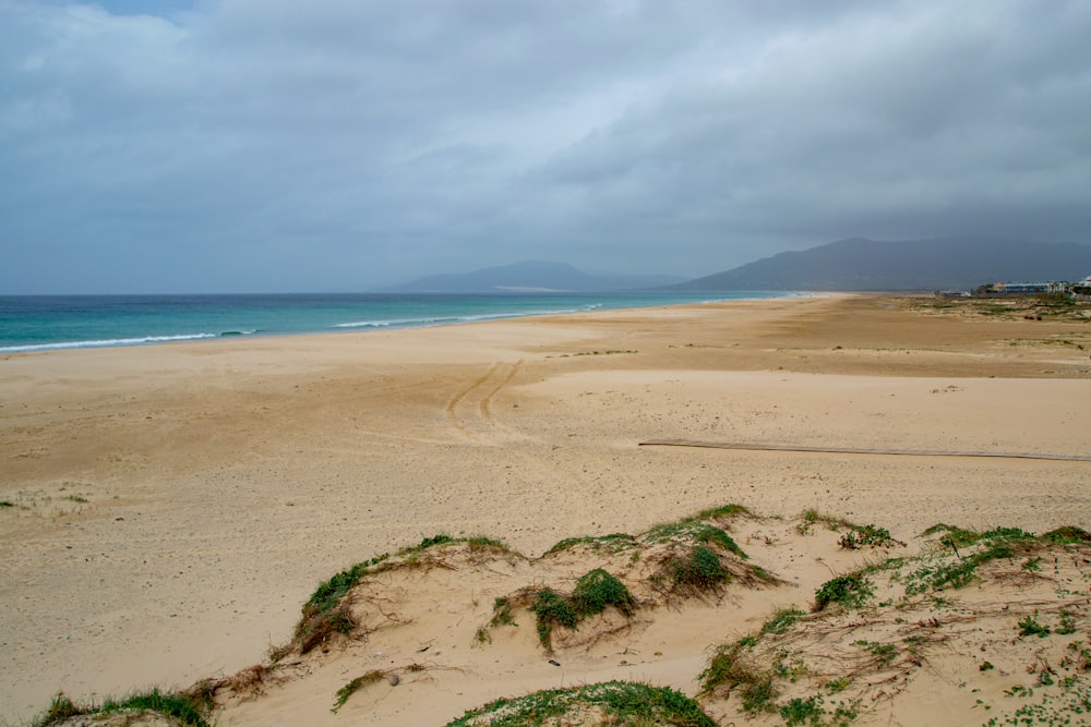 a sandy beach next to the ocean under a cloudy sky