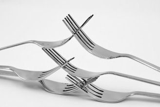A creative arrangement of four metal forks interlocked to form a balanced structure against a plain white background.