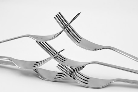 A creative arrangement of four metal forks interlocked to form a balanced structure against a plain white background.