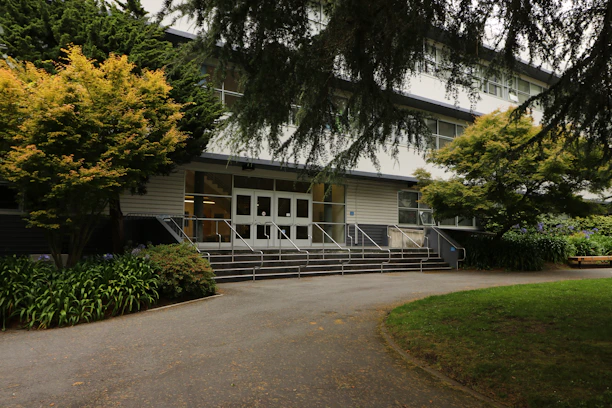 A calm residential building entrance with greenery and tidy pathways under soft morning light.