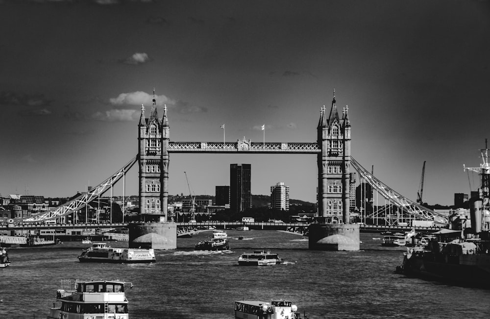 a black and white photo of boats in the water in front of a bridge