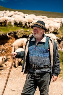 A weathered shepherd standing firm on a rugged hilltop, overlooking a scattered flock under a stormy sky.
