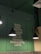 A green wall with a menu list featuring Italian food items such as pasta, pizza, risotto, lasagne, soups, gelato, tiramisu, panna cotta, and coffee. Three black pendant lights hang from the ceiling, casting a warm glow over the area. There is also a glimpse of some greenery in the form of palm leaves.