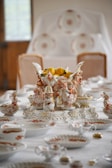 An ornate table setting with decorative porcelain figures and dishes, prominently featuring a centerpiece filled with lemons. The porcelain is detailed with red and gold accents set against a white background. The scene reflects an elegant dining room ambiance with soft lighting.