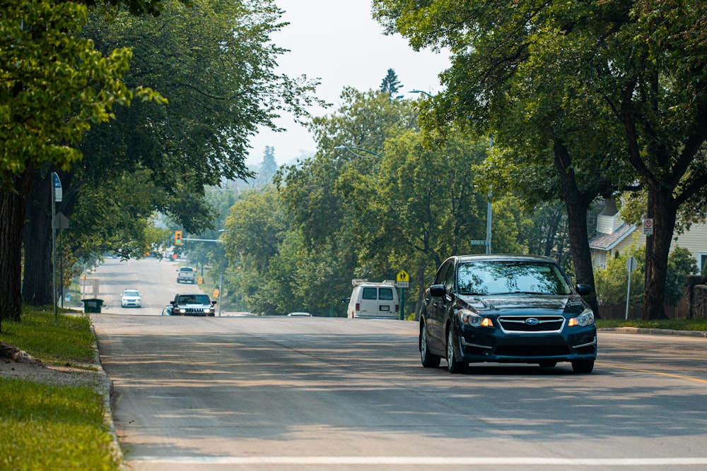 a black car driving down a tree lined street