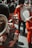 A group of people dressed in red military uniforms play musical instruments such as drums and brass horns. Their uniforms include tall, furry black hats, and the scene appears to be part of a ceremonial or parade event.