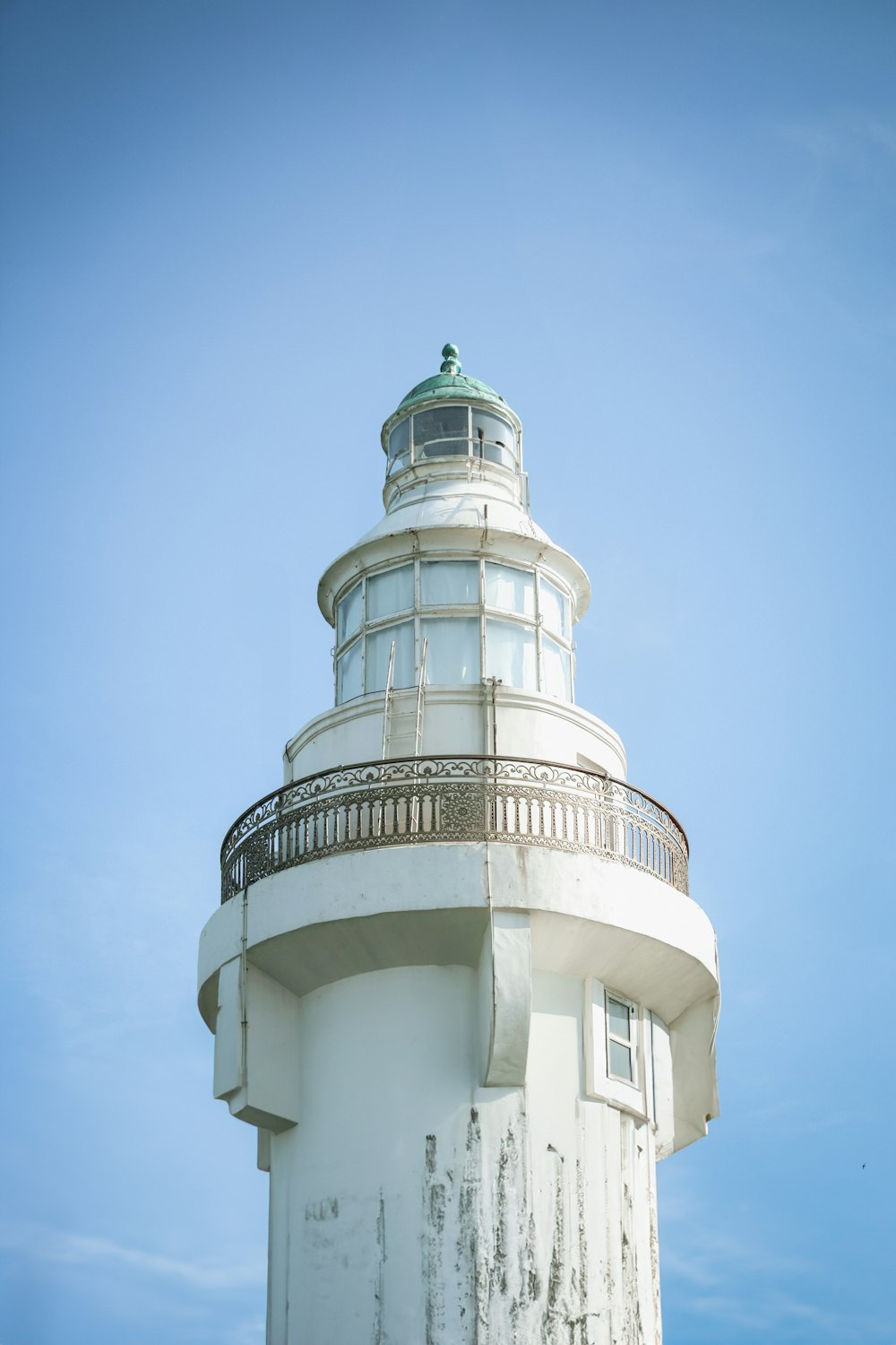 a white lighthouse with a green top against a blue sky