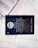 A dark-colored book titled 'De Volta ao Mosteiro' by James C. Hunter is lying on top of several open books with pages of text visible. The book cover features gold and white text along with an emblem or logo in white.