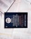 A dark-colored book titled 'De Volta ao Mosteiro' by James C. Hunter is lying on top of several open books with pages of text visible. The book cover features gold and white text along with an emblem or logo in white.